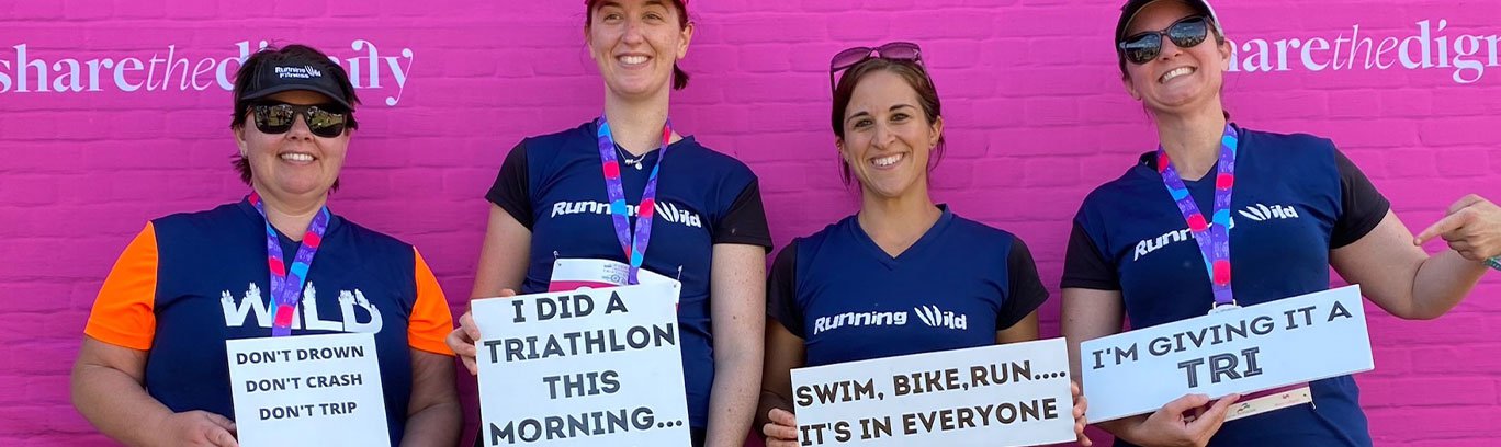 Four women holding triathlon signs in front of a pink wall